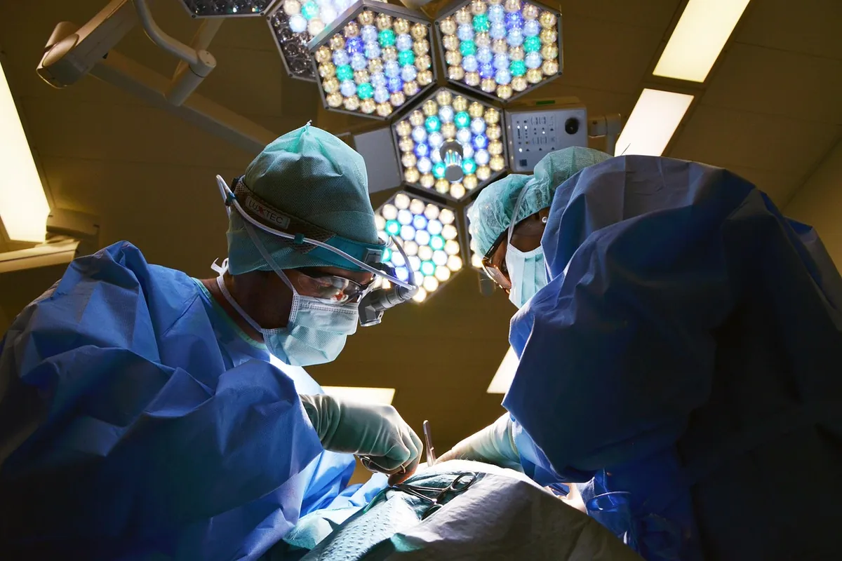 Cirurgião em sala de operação visto de baixo, sob focos de luz cirúrgica