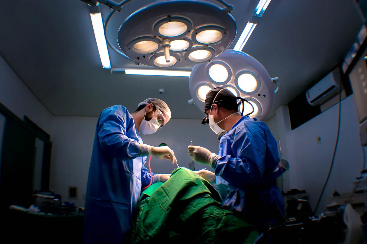 Dois cirurgiões operam um paciente sob focos de luz em uma sala cirúrgica