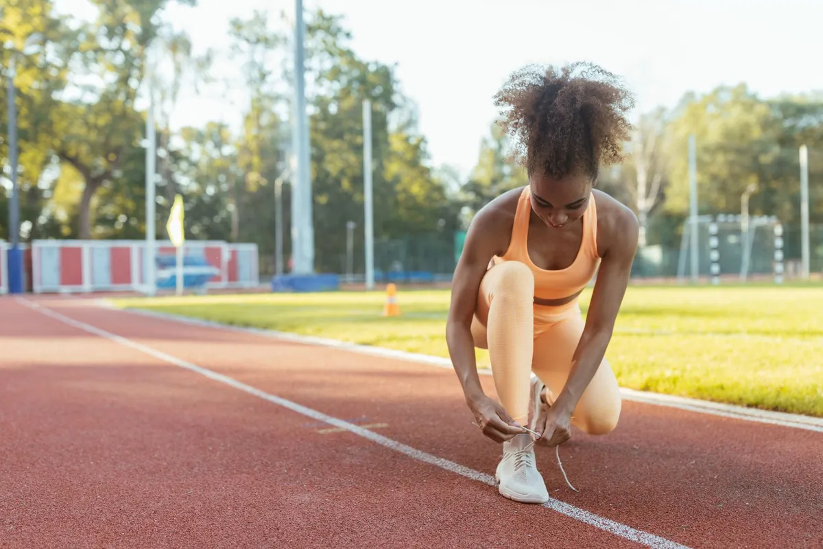 Corredora amarrando o tênis em uma pista de atletismo antes de treinar