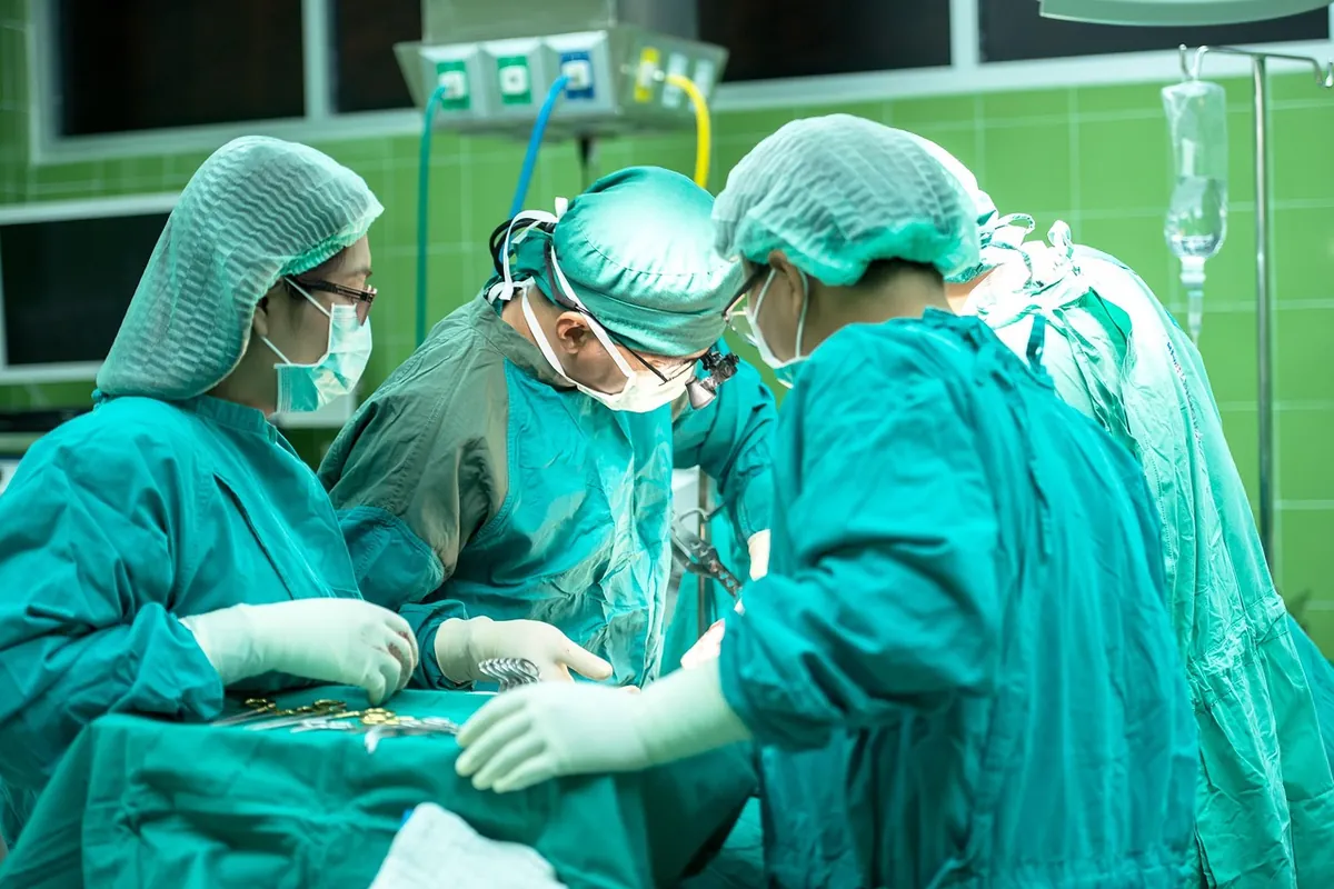 Equipe cirúrgica de máscara e gorro operando um paciente