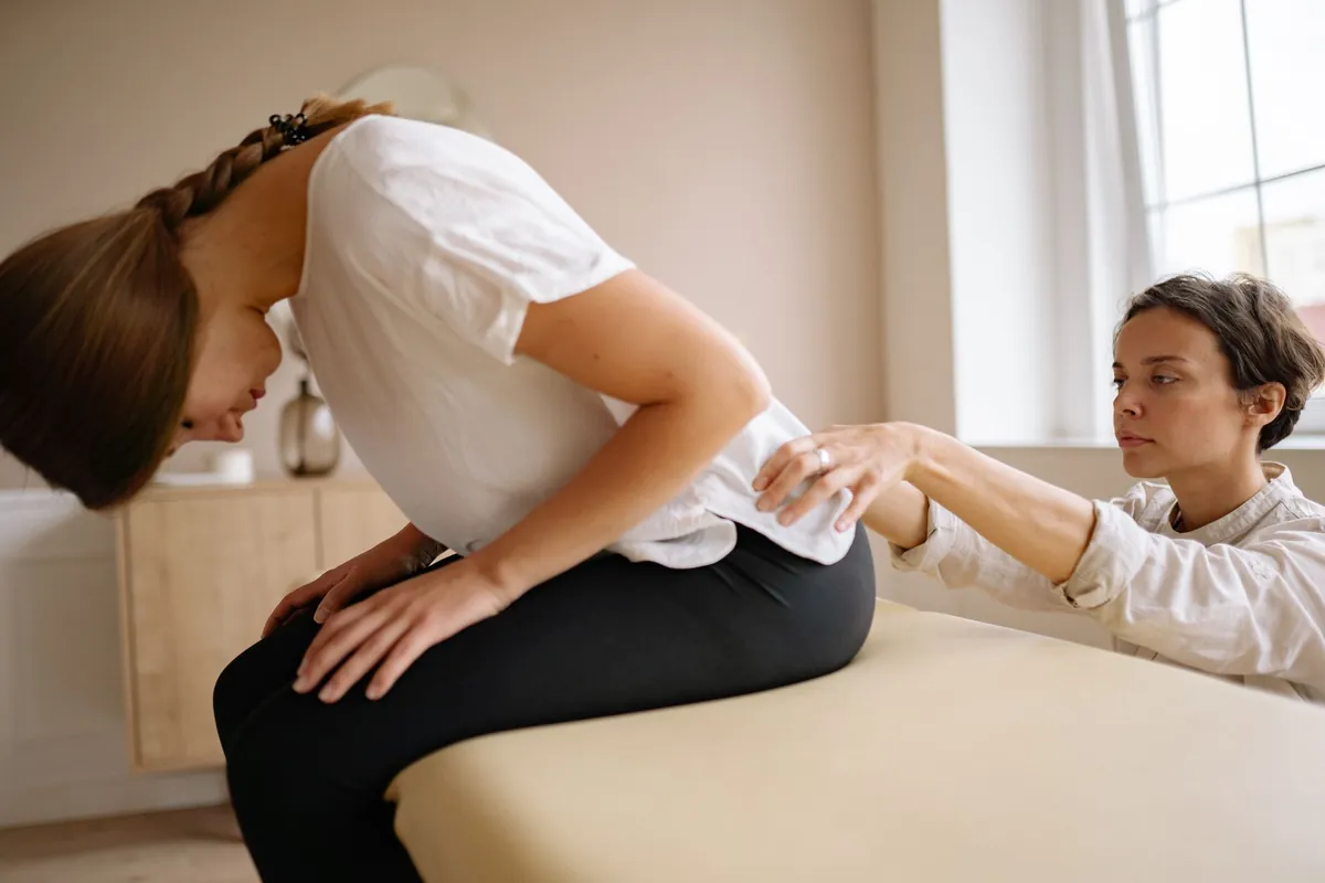 Fisioterapeuta avaliando uma mulher inclinada para a frente sentada em uma maca