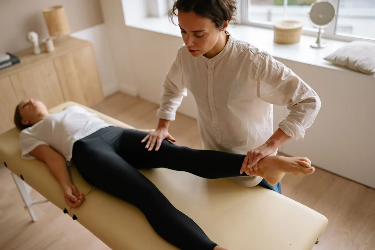 Fisioterapeuta orienta exercício de mobilidade da perna de uma mulher deitada em uma maca