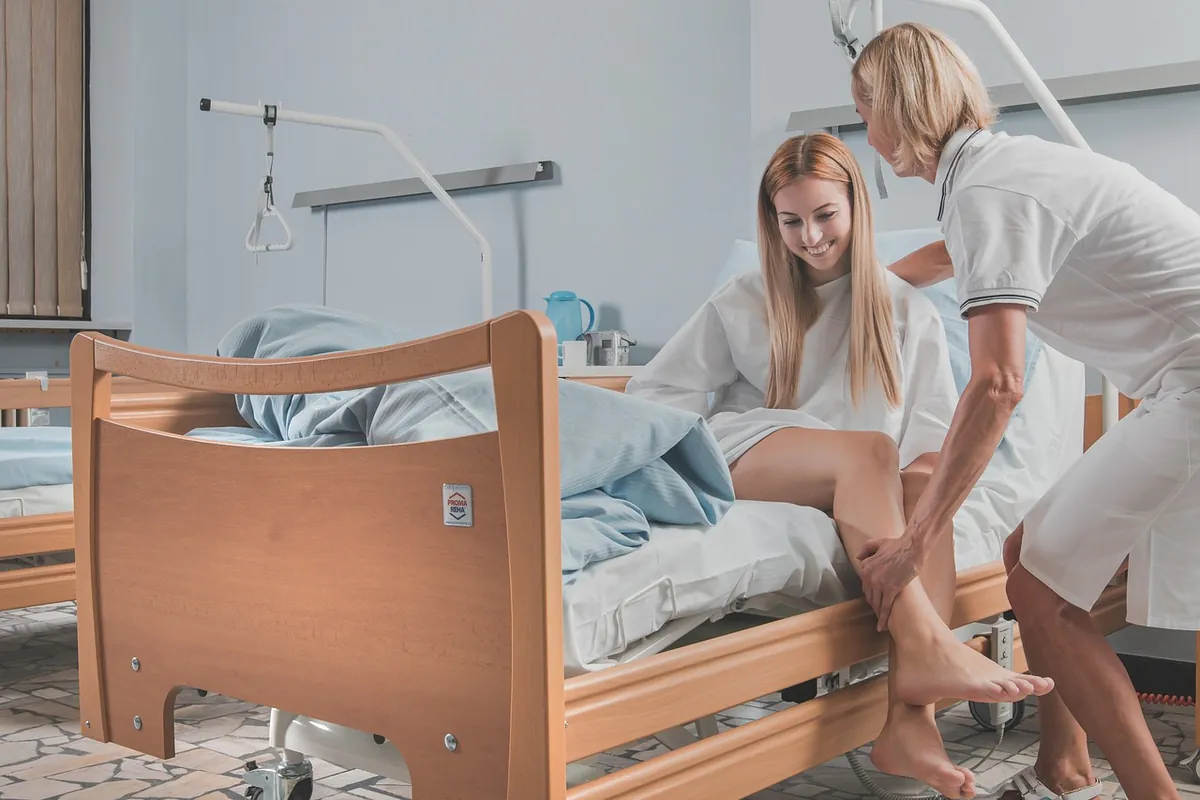Enfermeira ajudando uma paciente a se sentar na beira da cama do quarto