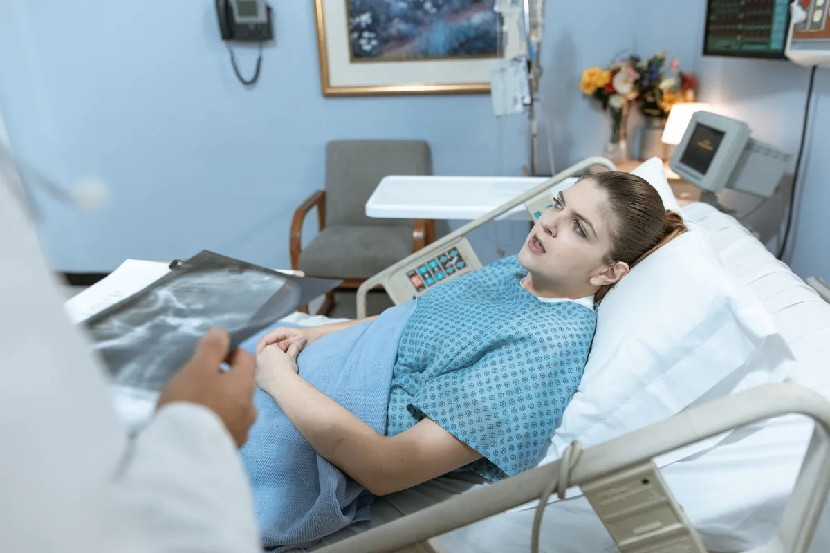 Paciente deitada em leito hospitalar enquanto um médico segura uma radiografia