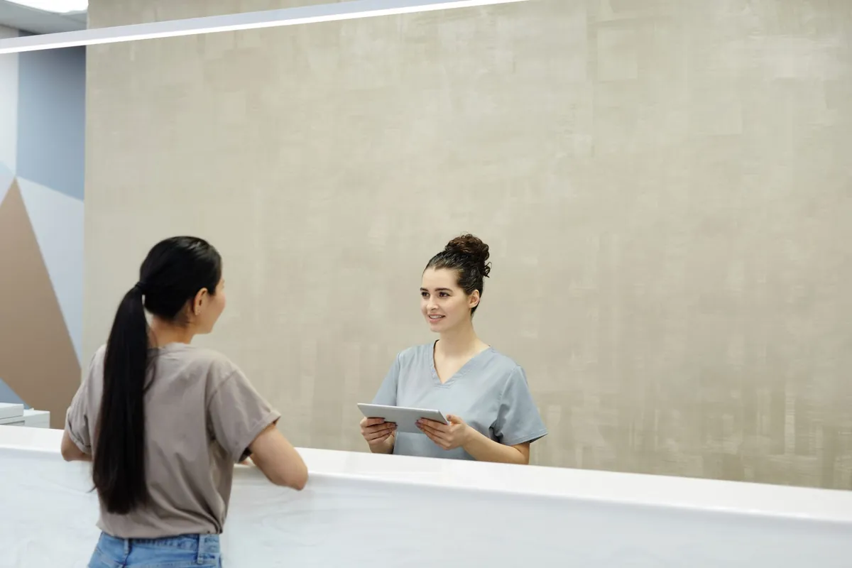 Atendente conversando com uma paciente no balcão de recepção de uma clínica